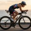 夕暮れの海岸線を、DHバーを装着したTT仕様のエアロロードバイクで疾走する日本人女性トライアスリート。ロードバイクのTT化カスタム、費用、互換性を解説するブログ記事のアイキャッチ画像。